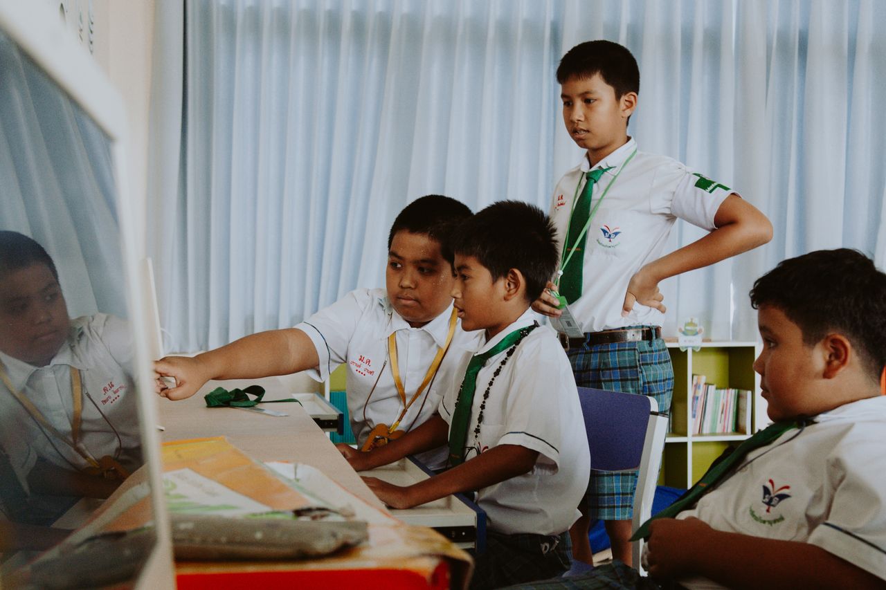 services-01 A group of boys in school uniforms collaborate on a computer project indoors.