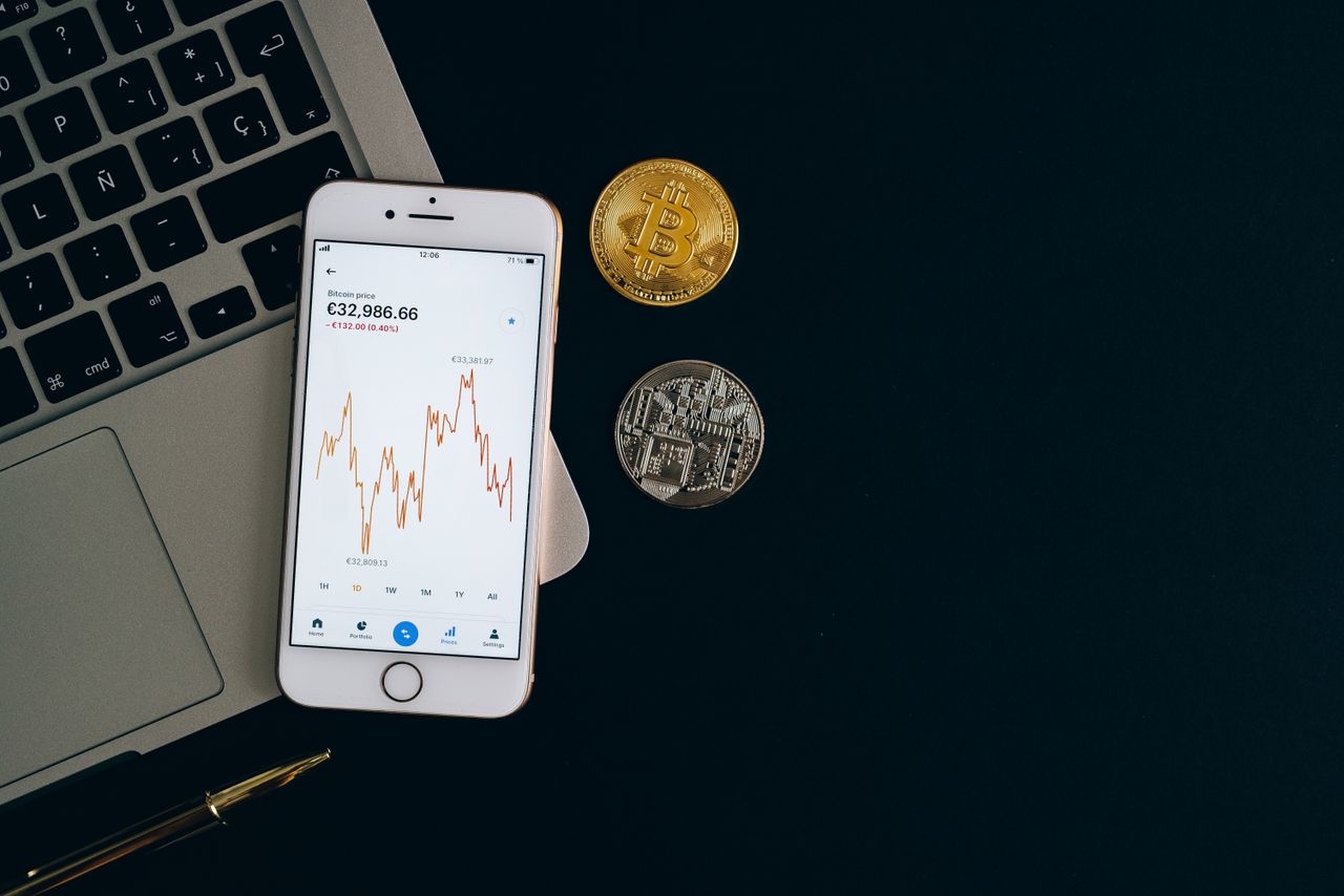 why-choose-us Smartphone displaying Bitcoin price chart alongside Bitcoin and Ethereum coins on black background.